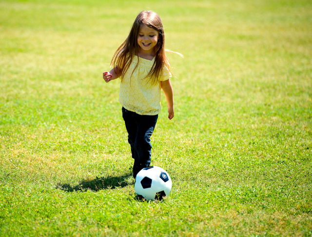 día del niño: niña con un balón de futbol en un campo de hierba