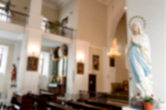 The statue of Mary against a column in a large empty white church with a chandelier and paintings in the background