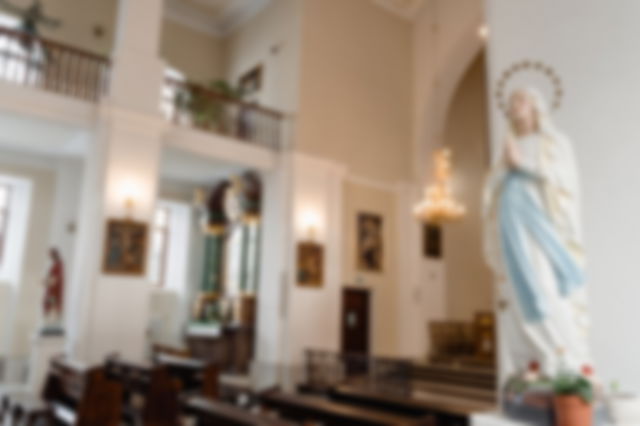 The statue of Mary against a column in a large empty white church with a chandelier and paintings in the background