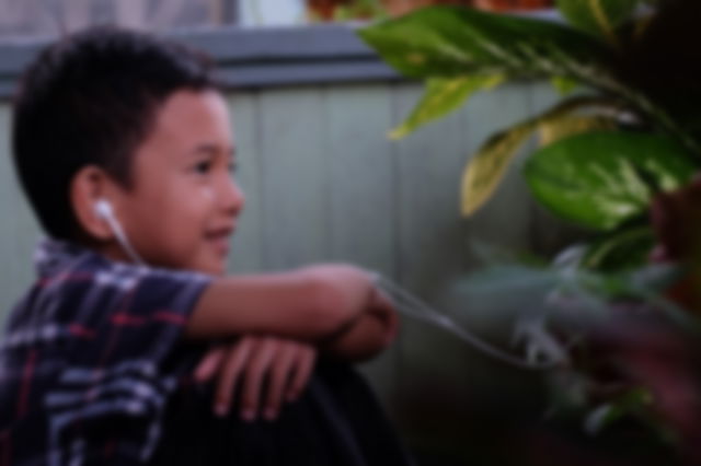 niño con auriculares contemplando sonriente una planta