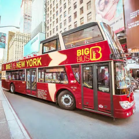 A red double-decker sightseeing bus labeled &ldquo;Big Bus New York&rdquo; parked along a busy city street, with pedestrians on the sidewalk and tall skyscrapers and digital billboards surrounding the scene.