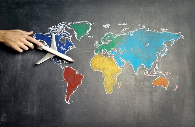 A world map on a chalkboard, a toy plane is held against North America by the index finger of a hand