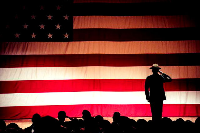 Soldier saluting on stage in front of a large American flag