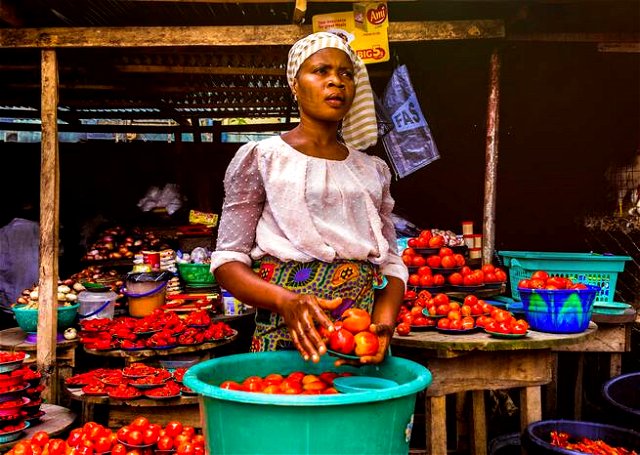 African woman in a market holding a plate of tomatoes