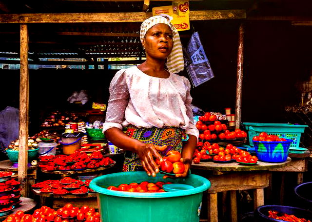 African woman in a market holding a plate of tomatoes