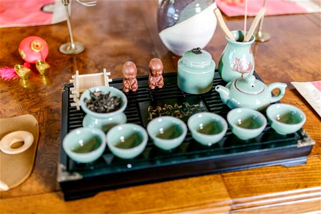 A tray of teal pots and cups of tea in an ancient ceremony. Two mini statues of buddha on the tray