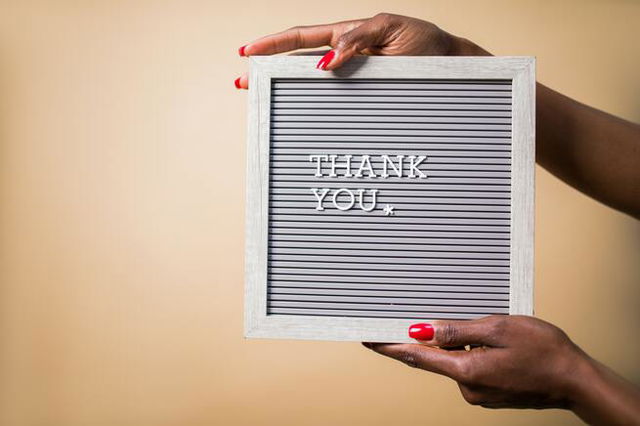 A woman off screen holding a sign which says Thank You. She is wearing red nail varnish