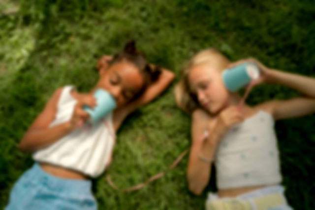 Two Teenage Girls Laying on Grass and Playing Telephone Call Using Plastic Cups