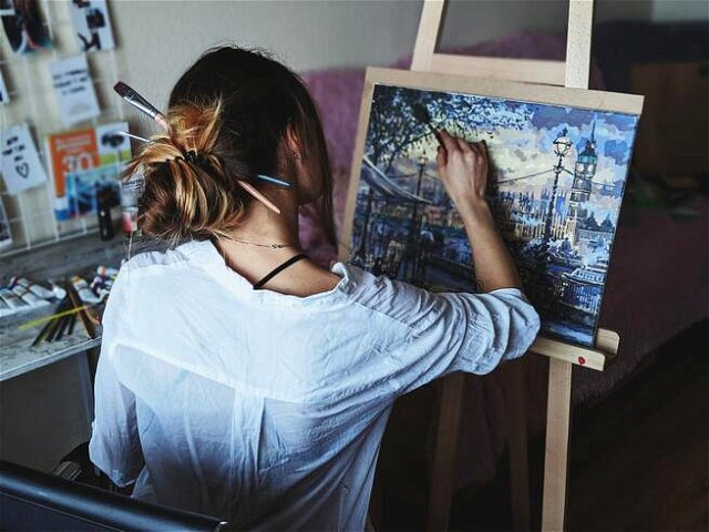 With their back to a camera, an artist paints a city scene on an easel