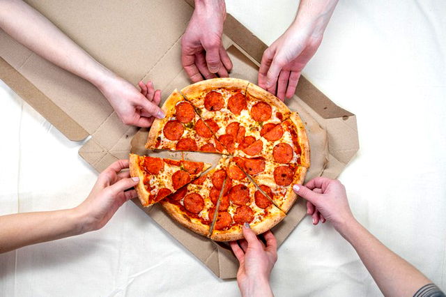 Pizza resting in a takeaway box, six arms each reaching for a slice from different directions.