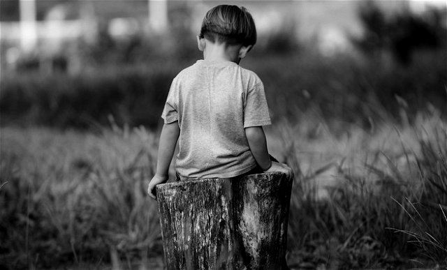 Criança sentada em tronco de árvore cortado, de costas