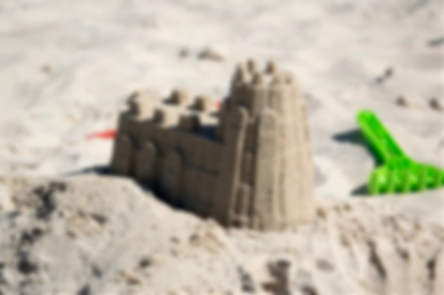 Close-up of a sandcastle with a green plastic beach fork beside it