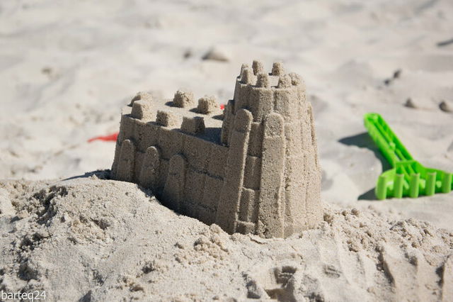 Close-up of a sandcastle with a green plastic beach fork beside it